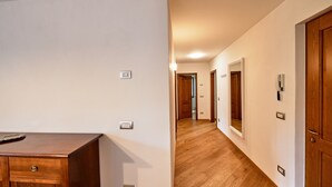 Un pasillo con suelo de madera, paredes blancas y puertas con interruptores de luz.