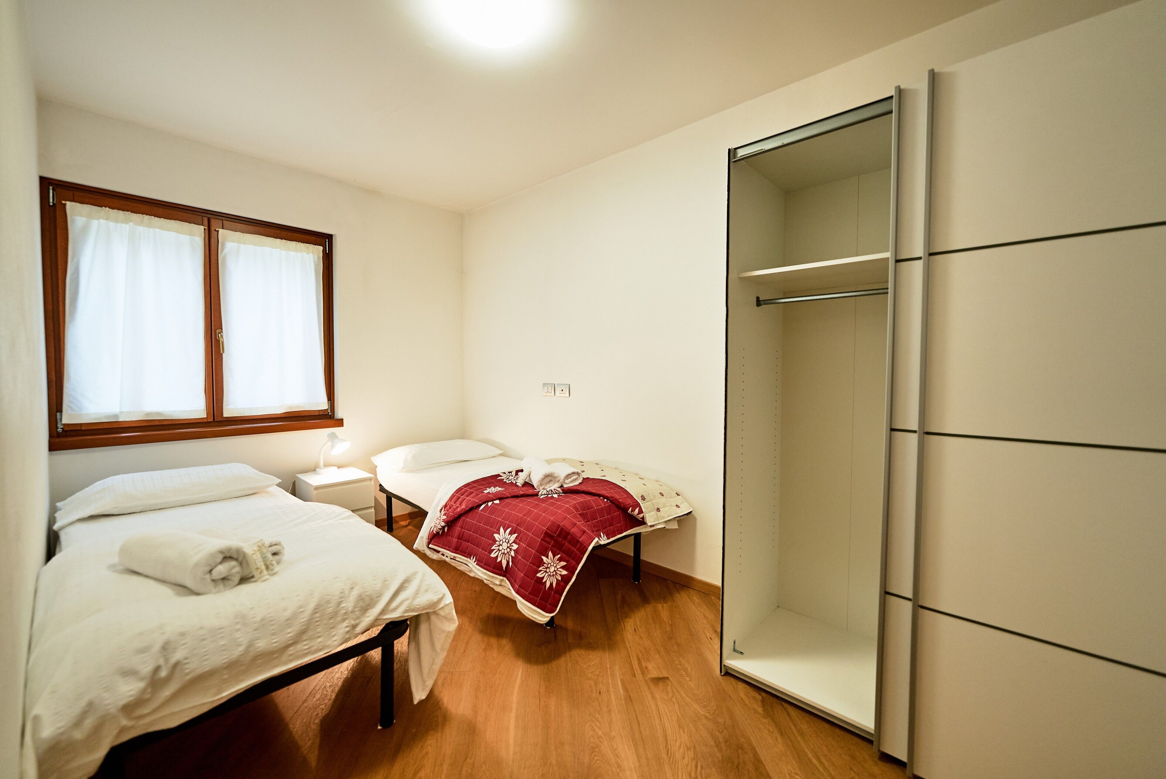 Een slaapkamer met twee bedden, een kledingkast en een raam met gordijnen.
