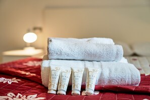 A neatly arranged set of toiletries on a bed with a red patterned bedspread. - Dolomis Apartments Rododendro 6 Guests (Caderzone Terme)