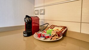 Una cafetera, un hervidor rojo y una bandeja con tazas de café y bizcochitos sobre una encimera de cocina.