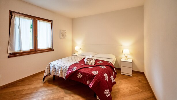 Un dormitorio con cama, dos mesitas de noche, una ventana con cortinas y una decoración de corazón en la pared.
