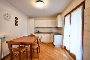 A compact kitchen with white cabinets, a wooden dining table with chairs, and a built-in oven. - Dolomis Apartments Rododendro 6 Guests (Caderzone Terme)