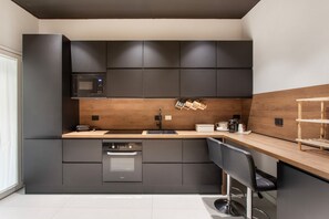 A modern kitchen with dark cabinetry, a built-in microwave, a coffee machine, and a wooden countertop. - Bed and Breakfast "Camera 102" with Balcony, Wi-Fi and Air Conditioning (Catania)