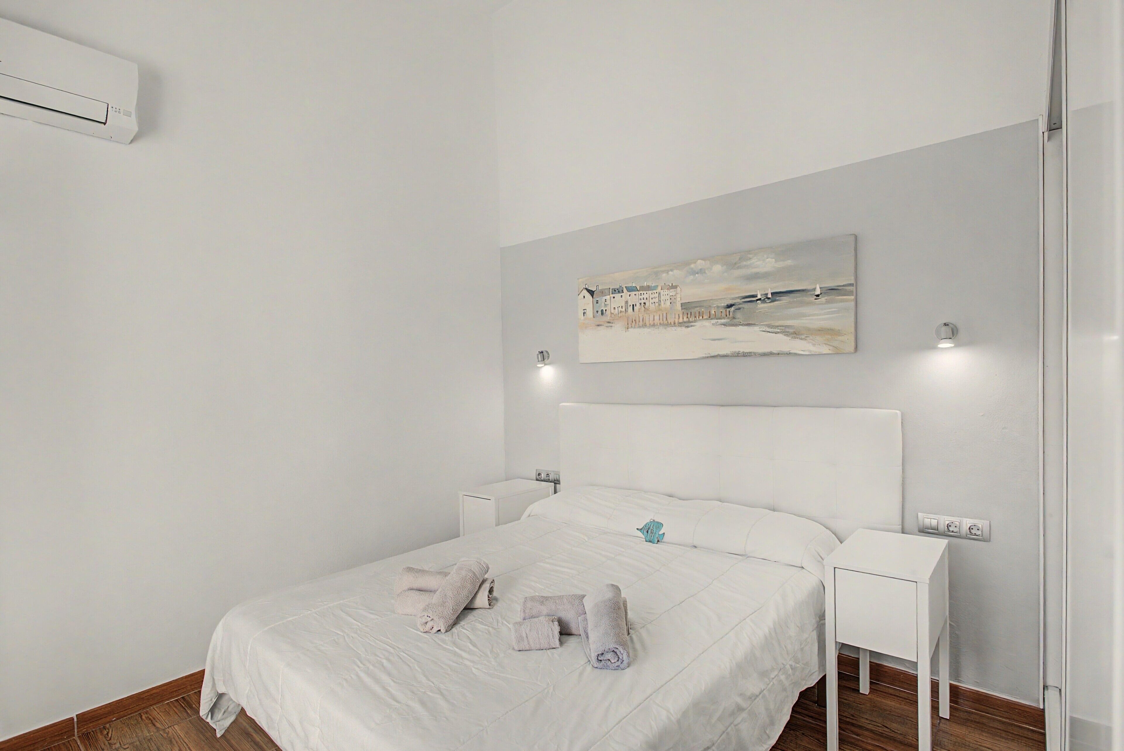 Ein Hotelzimmer mit einem Bett, einem Gemälde, Nachttischen und einer Klimaanlage.