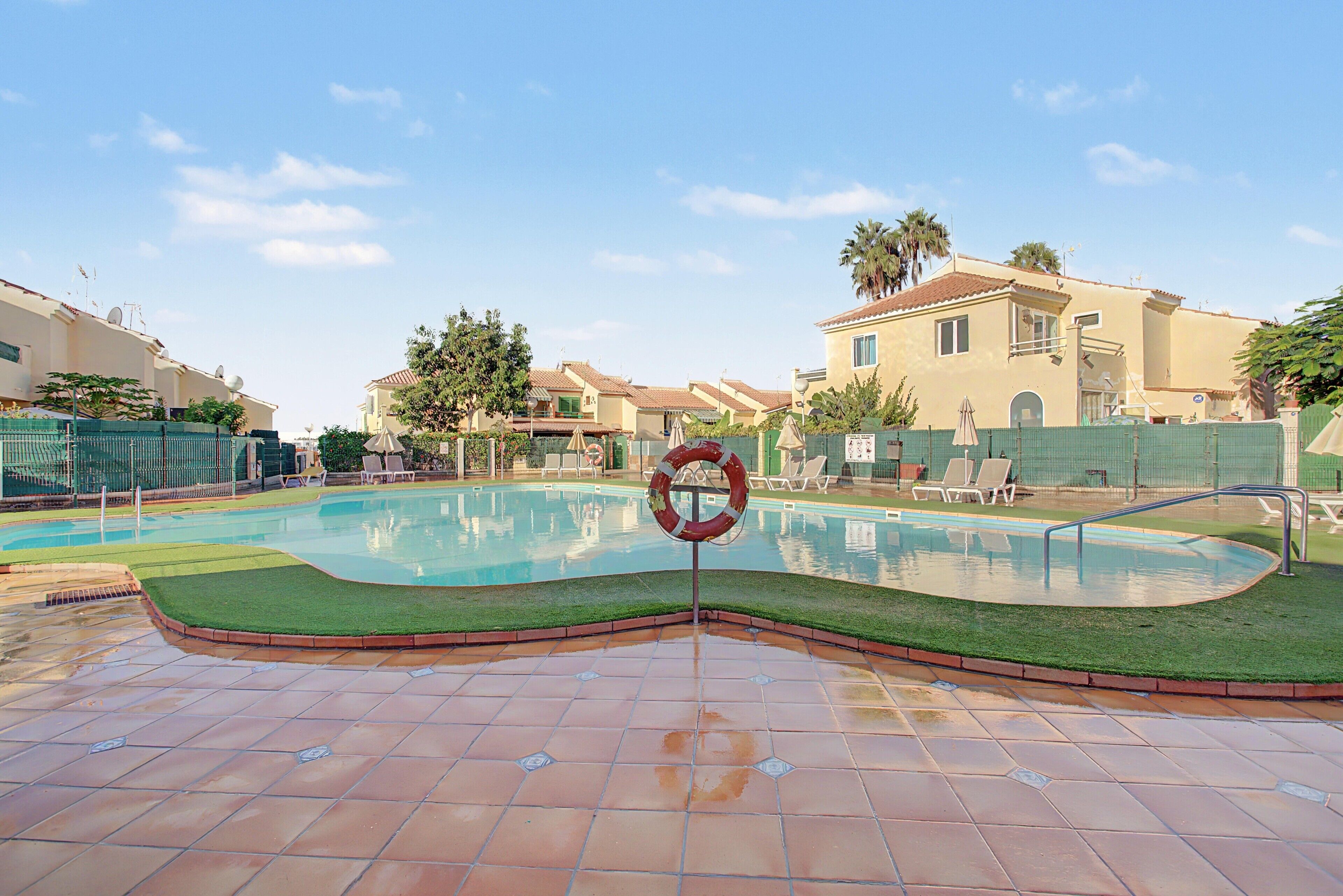 A swimming pool with a lifebuoy, surrounded by a green fence, and adjacent buildings.