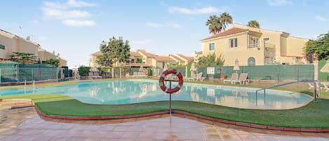 Piscina com boia salva-vidas, cercada por um muro verde e edifícios próximos.