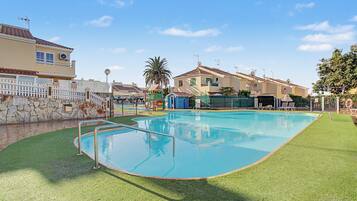 Ein Swimmingpool mit einer umliegenden Rasenfläche, einer Palme und einem Gebäude mit einem Ziegeldach.