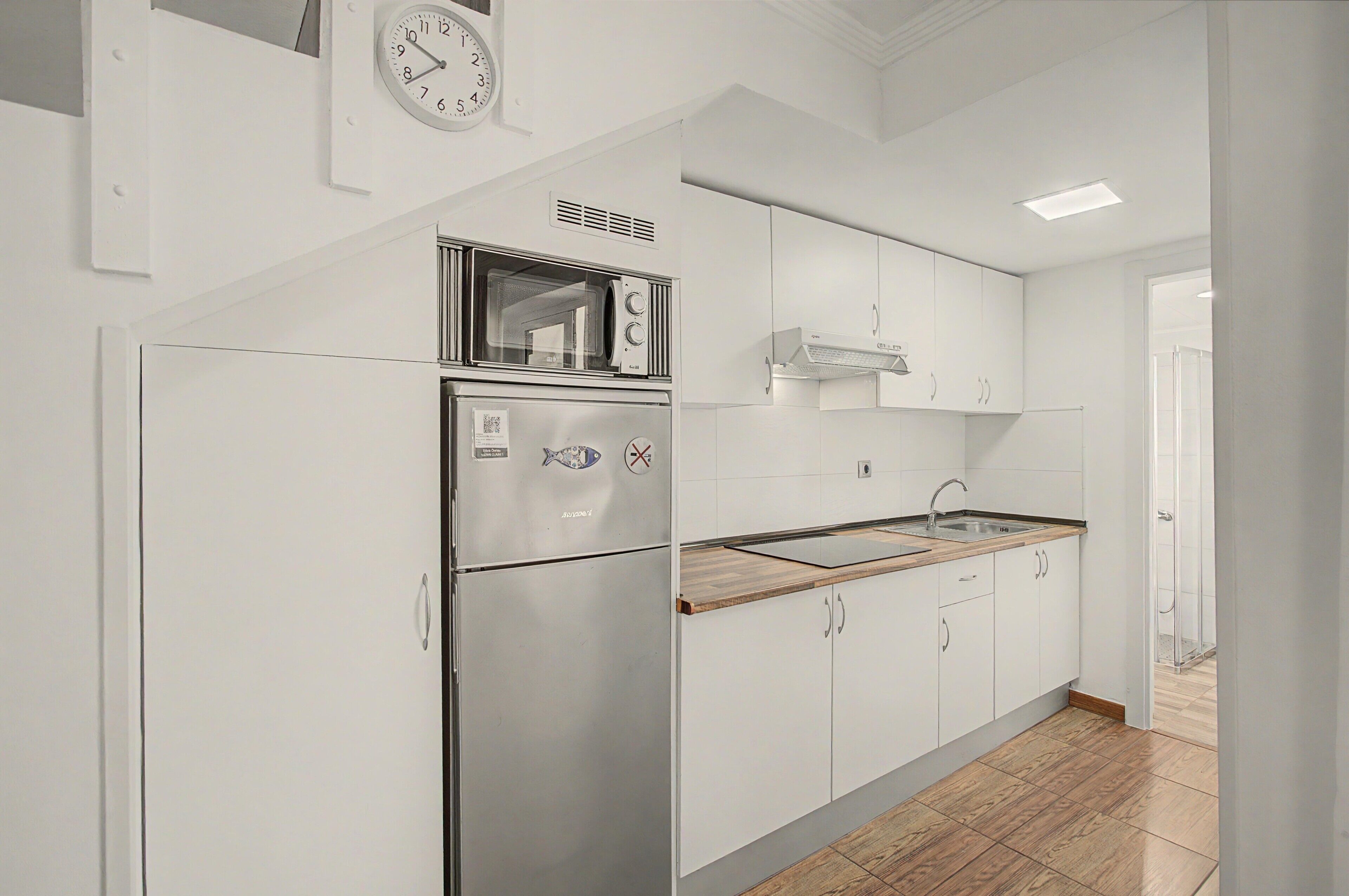 Een moderne keuken met witte kasten, een ingebouwde magnetron en een roestvrijstalen koelkast.