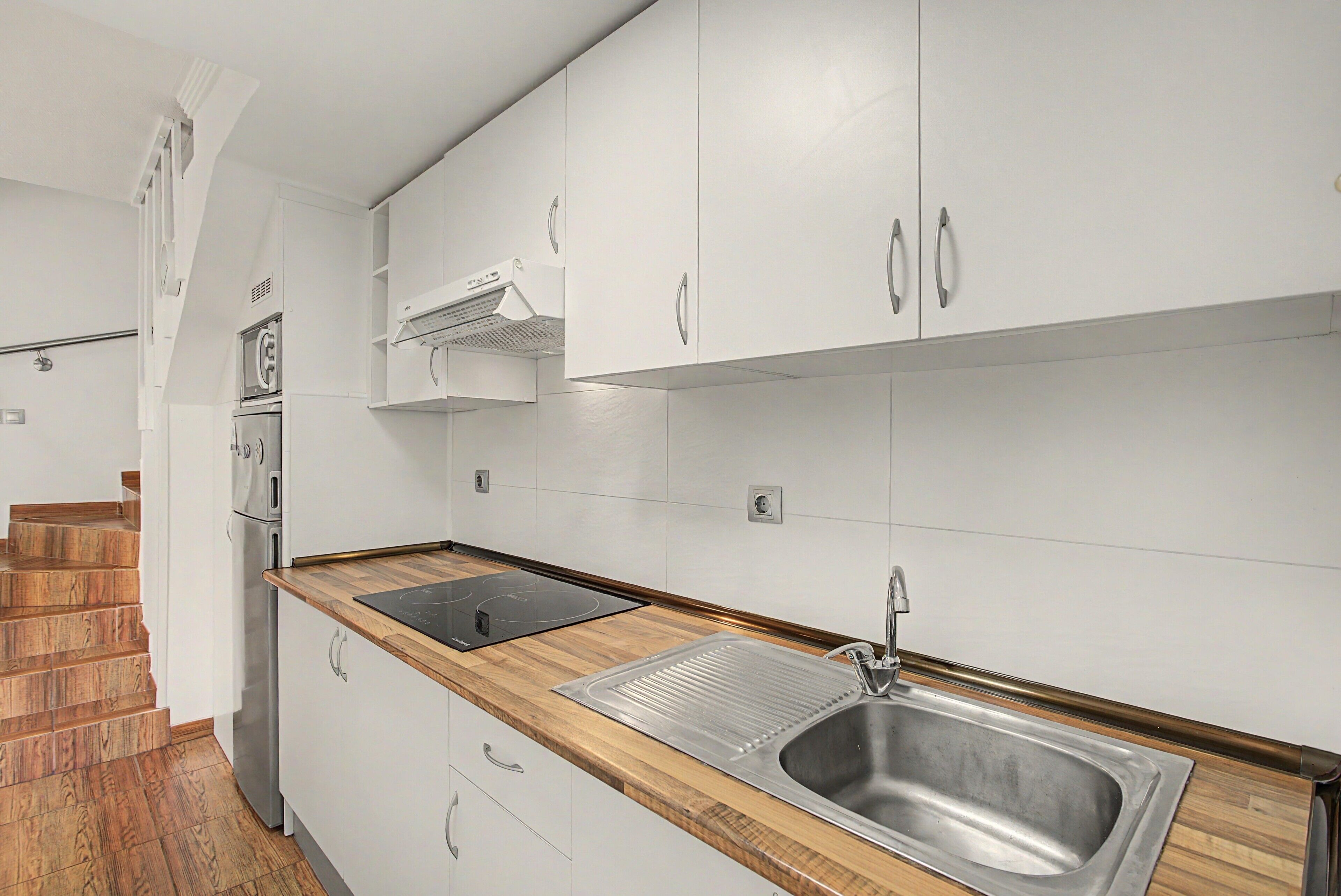 Une cuisine moderne avec des meubles blancs, un évier en acier inoxydable et un plan de travail en bois.