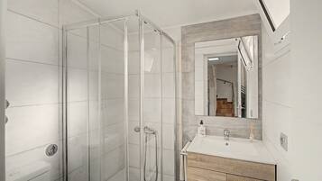 Een moderne badkamer met een douchecabine van glas, een witte wastafel met houten kastje en een spiegel met houten lijst.