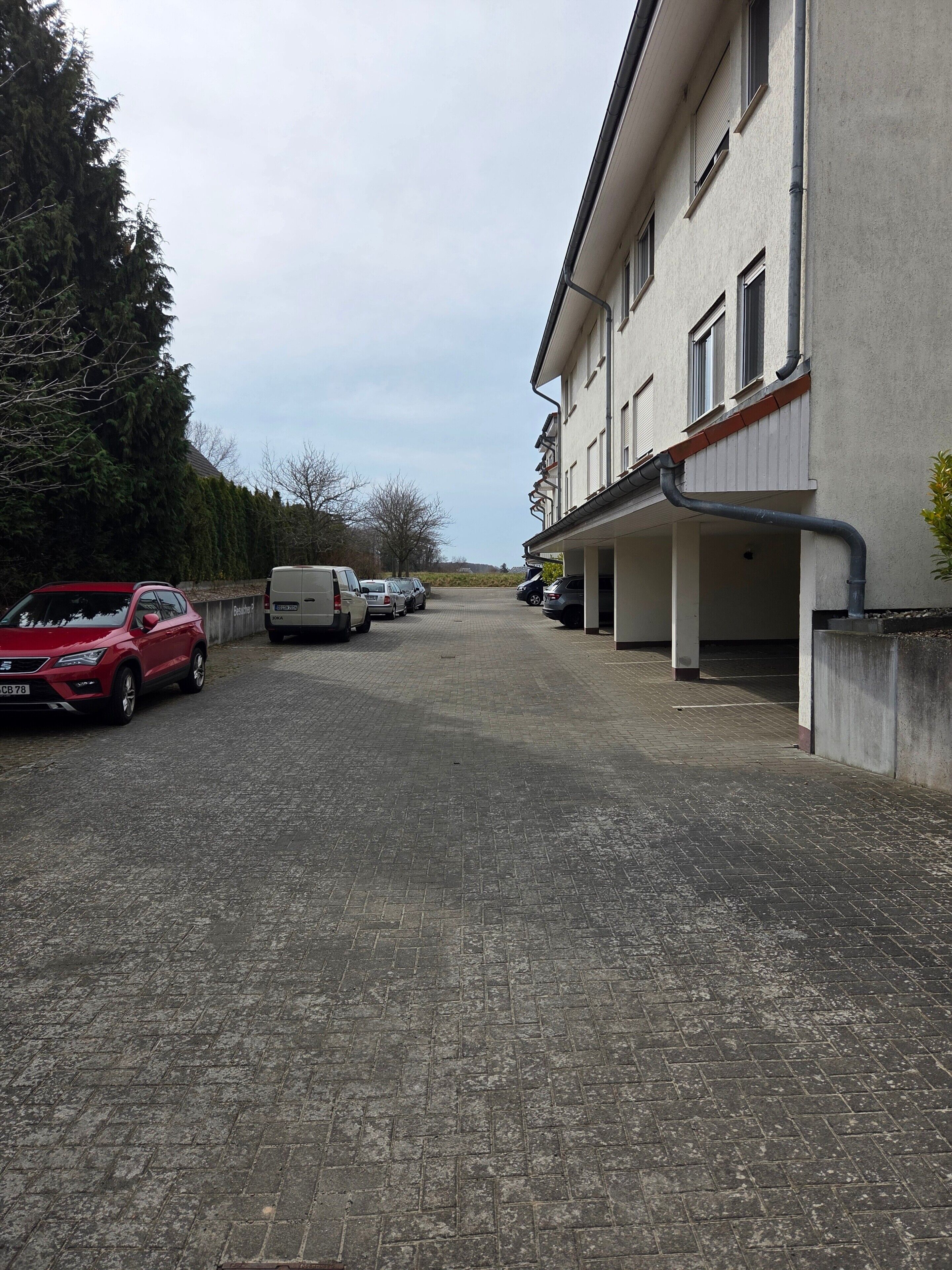 A parking area with multiple cars and a building with a flat roof and a covered walkway.