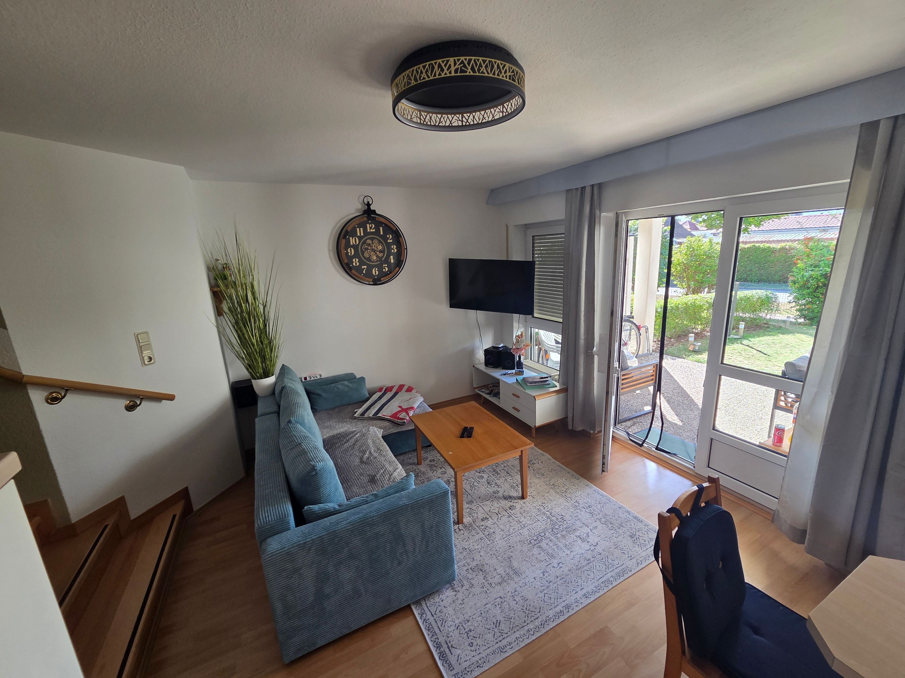 Ein Wohnzimmer mit einer Couch, einem Couchtisch, einem Fernseher und einem großen Fenster mit Blick ins Freie.