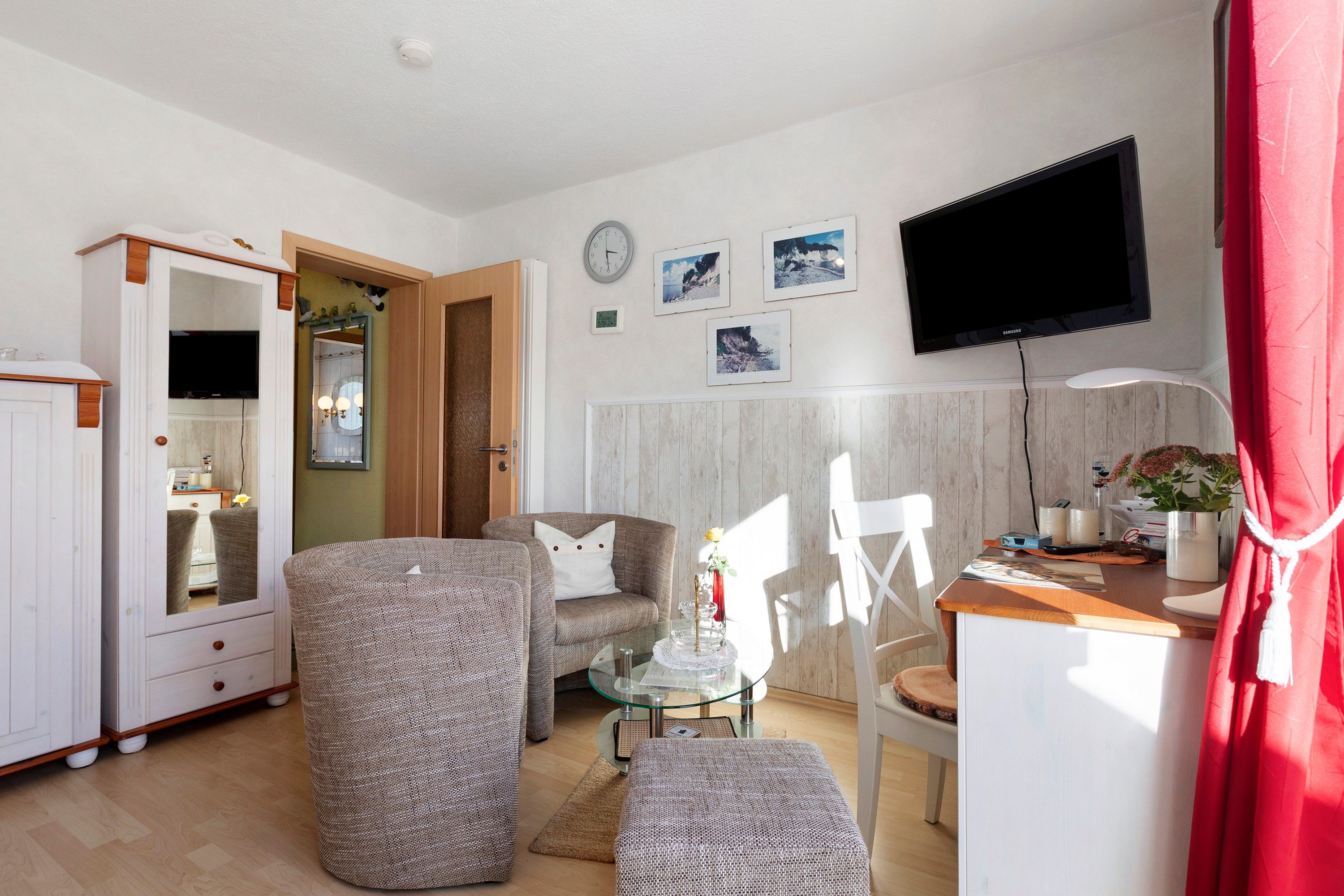 Ein Wohnzimmer mit einer Couch, einem Hocker und einem Fernseher an der Wand.