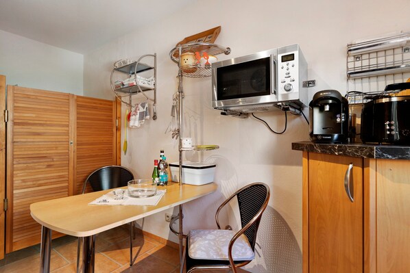 A compact kitchen with a microwave, coffee maker, and a hanging rack with kitchen utensils.