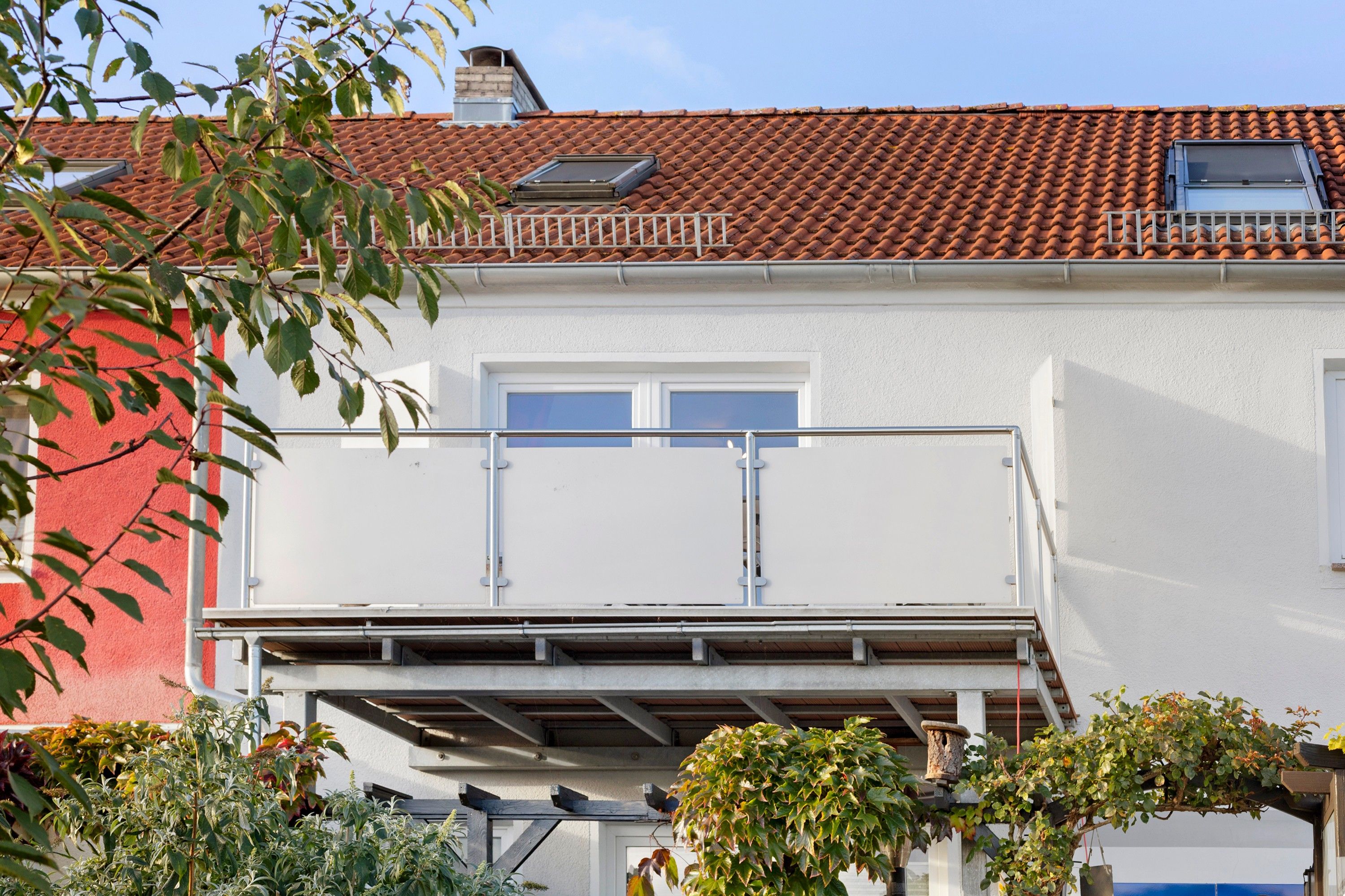 Ein zweistöckiges Gebäude mit rotem Ziegeldach, weißen Wänden und einem Balkon mit Metallgeländern.