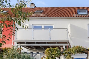 A two-story building with a red-tiled roof, white walls, and a balcony with metal railings.
