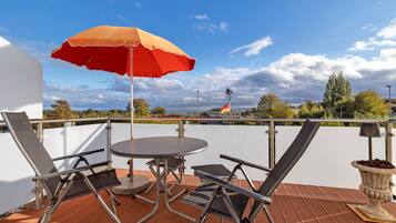 A balcony with a table and chairs, a red umbrella, and a view of the cityscape.
