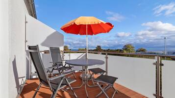 A balcony with a table and chairs, a red umbrella, and a view of the sea.