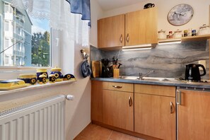 A compact kitchen with wooden cabinets, a marble backsplash, and a window with lace curtains.