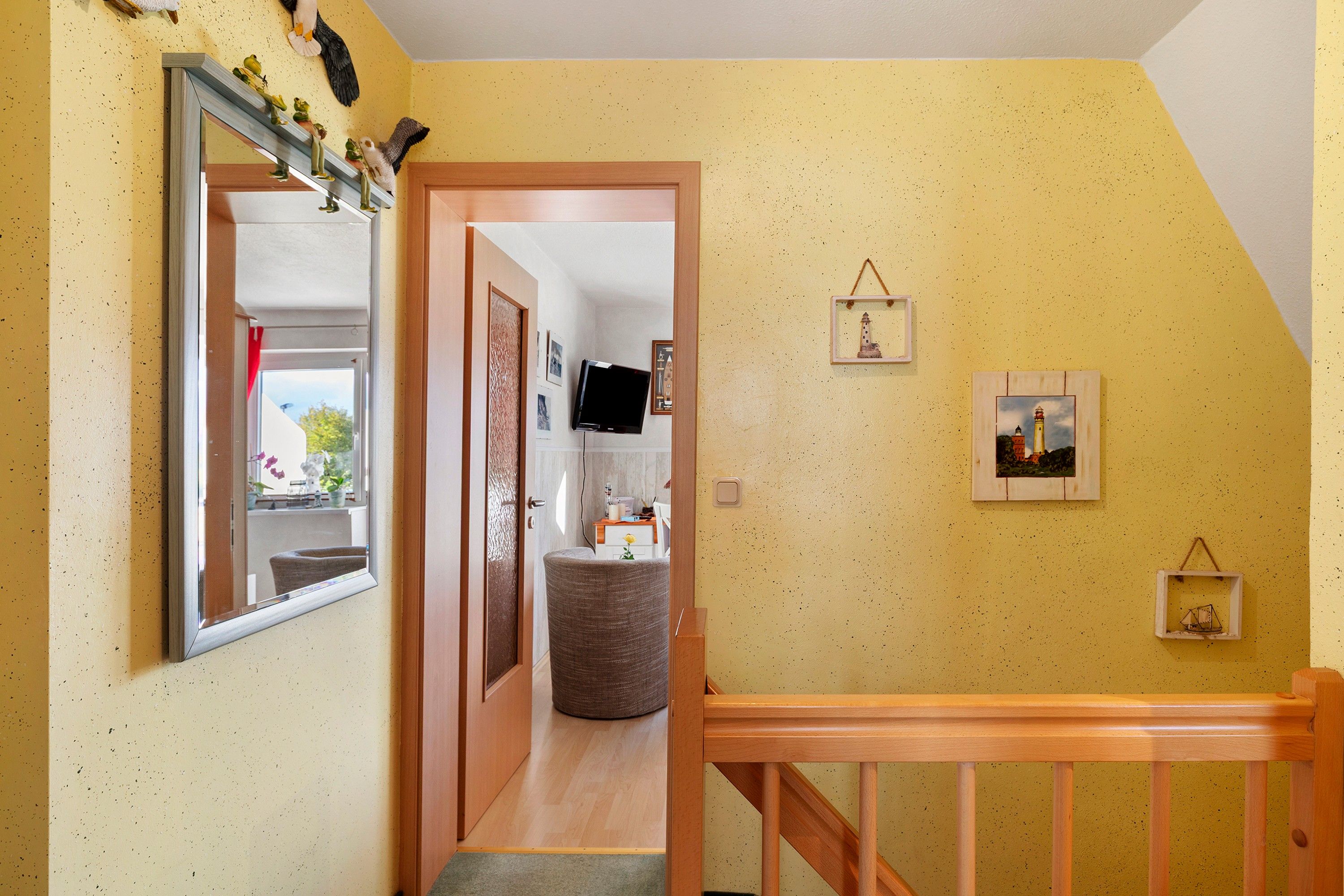 Ein Flur mit einer Holztreppe, einem Spiegel und einer Tür zu einem Raum mit Fernseher und kleinem Tisch.