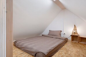 Habitación pequeña con techo inclinado, una cama, una mesita de noche y una lámpara de pared.