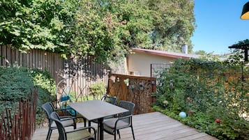 Une terrasse en bois avec une table et des chaises, entourée d’une clôture en bois et d’une végétation luxuriante.