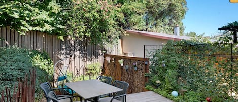 A wooden deck with a table and chairs, surrounded by a wooden fence and lush greenery.