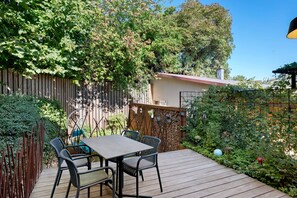 Una terraza de madera con una mesa y sillas, rodeada por una valla de madera y abundante vegetación.