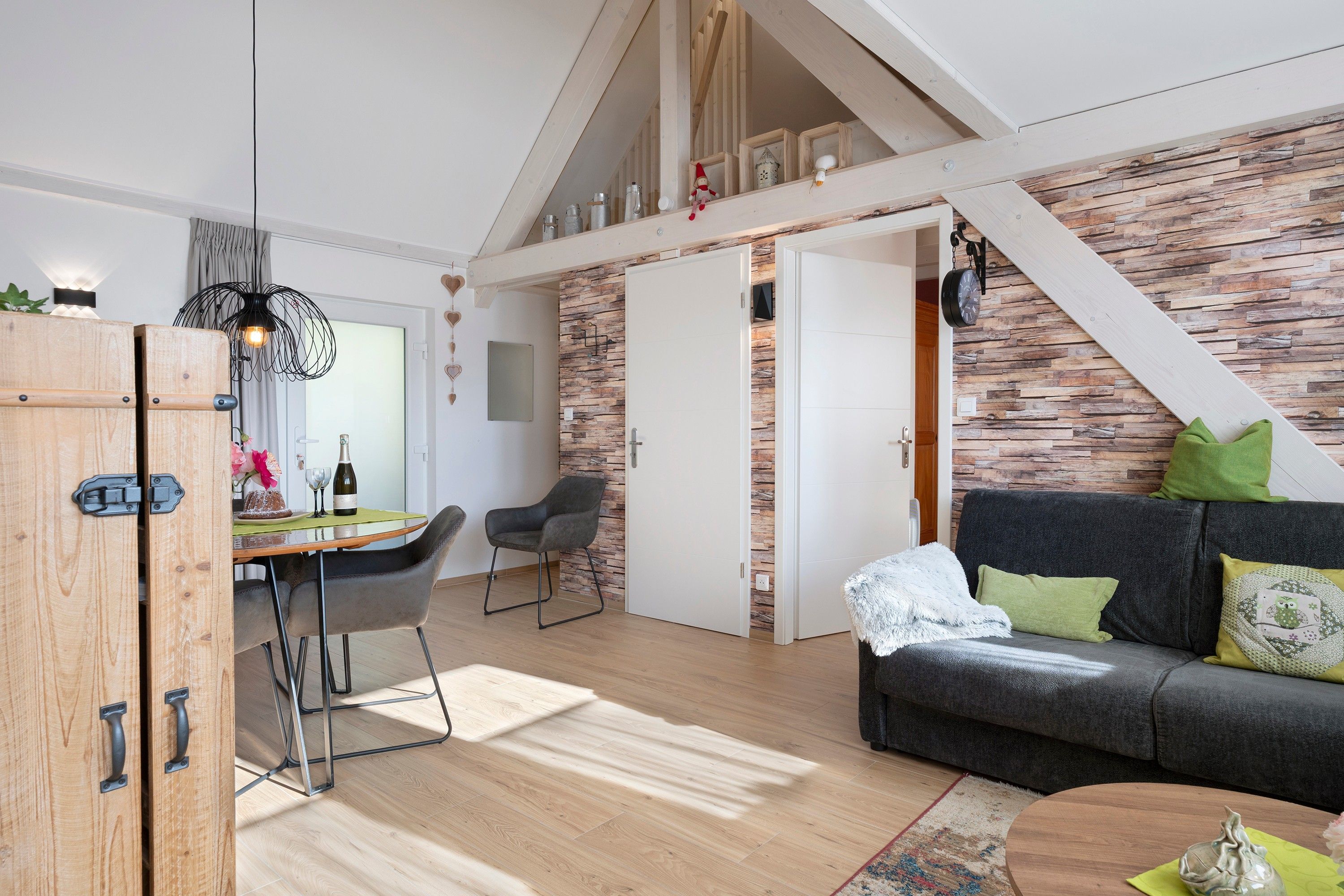 Un salon chaleureux avec un canapé gris foncé, une table à manger en bois avec des chaises et un escalier menant à l’étage supérieur.