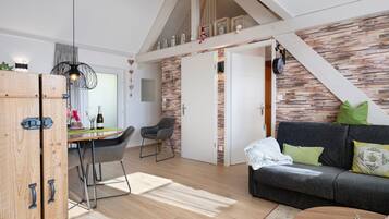 Un salon chaleureux avec un canapé gris foncé, une table à manger en bois avec des chaises et un escalier menant à l’étage supérieur.