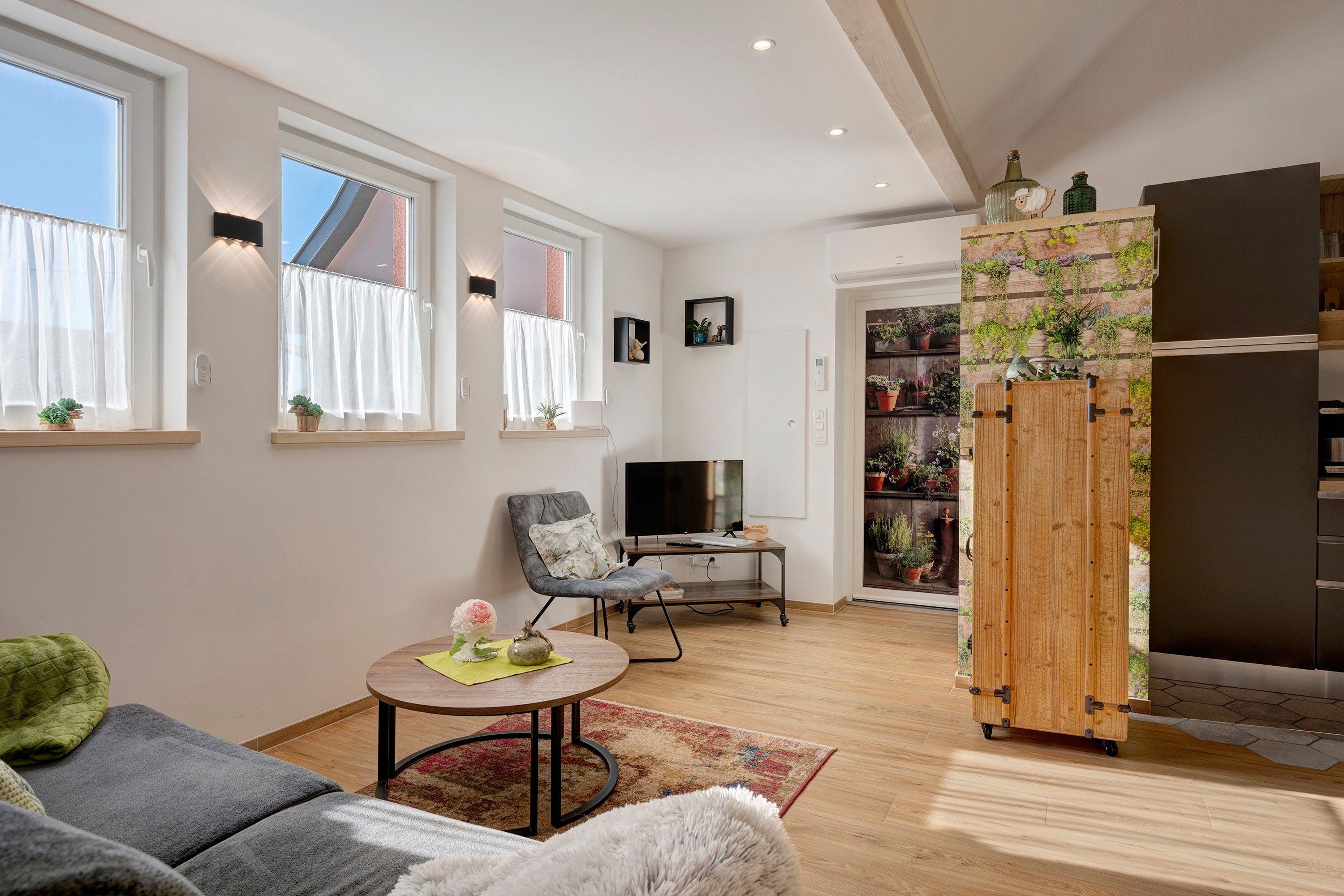 Un salon moderne avec un canapé, une table basse ronde, un téléviseur et un meuble en bois agrémenté de plantes.
