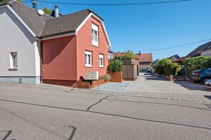 A residential street with houses, a gravel driveway, and parked cars.