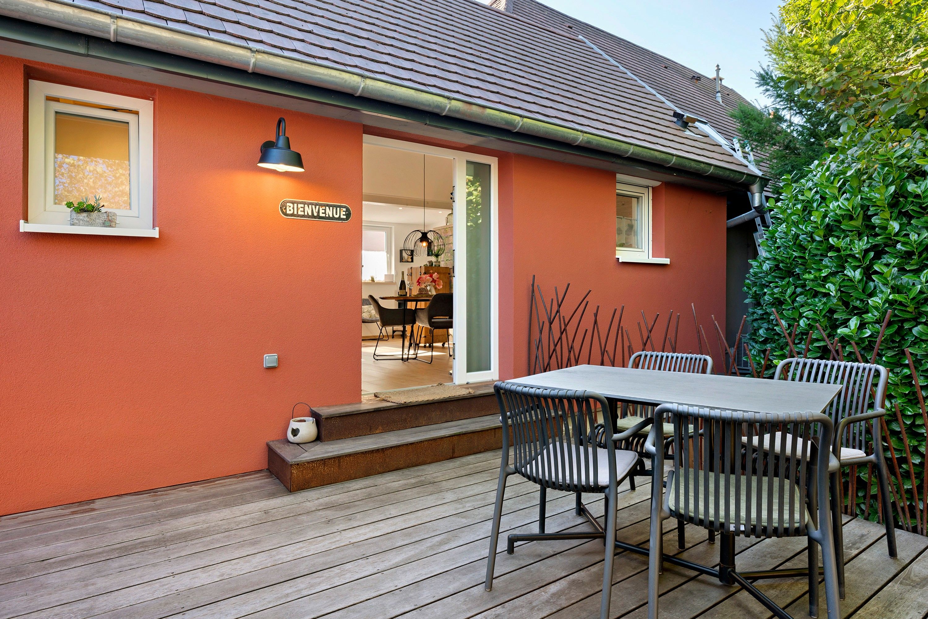 A red building with a sign reading 'BIENVENUE' and a patio area with a table and chairs.