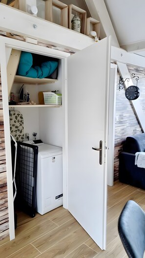 A room with a white door, a washing machine, a drying rack, and a small shelf with a decorative item.