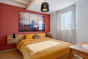 A hotel room with a bed, a nightstand, a lamp, a painting, and a window with curtains.