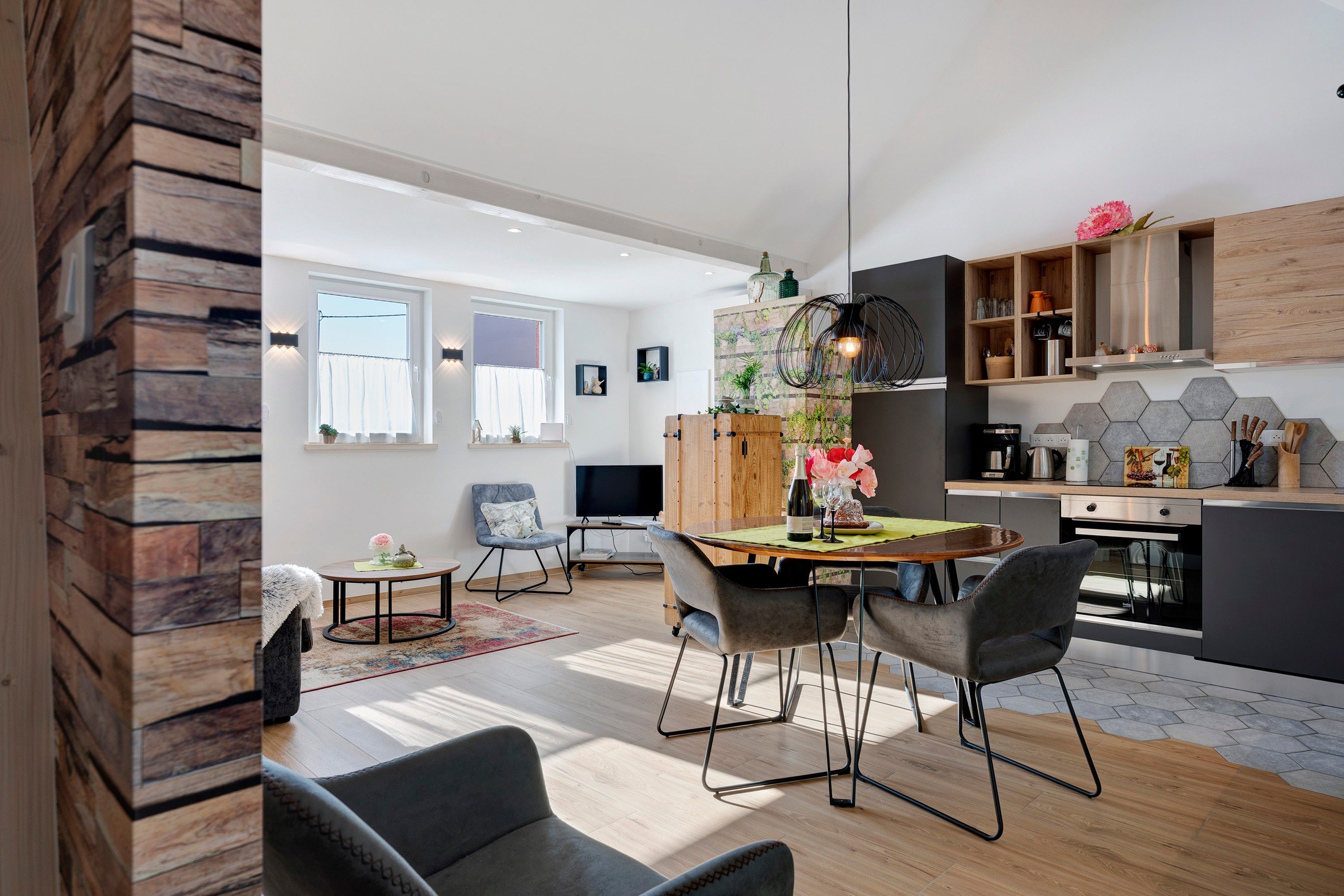 Et moderne køkken med træskabe, et spiseområde med bord og stole, samt en stue med sofa og fjernsyn.