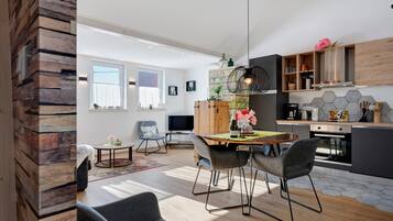 Et moderne køkken med træskabe, et spiseområde med bord og stole, samt en stue med sofa og fjernsyn.