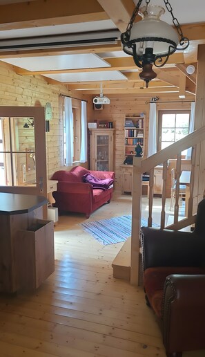 A wooden interior with a red sofa, a bookshelf, and a staircase. - Lärchenhütte Holiday Home with Infrared Sauna, Terrace, Garden – Sleeps 8 (Sankt Kathrein am Offenegg)