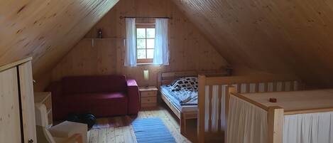 A small, wooden attic room with a sloped ceiling, a red sofa, a single bed, a nightstand, and a window with curtains.