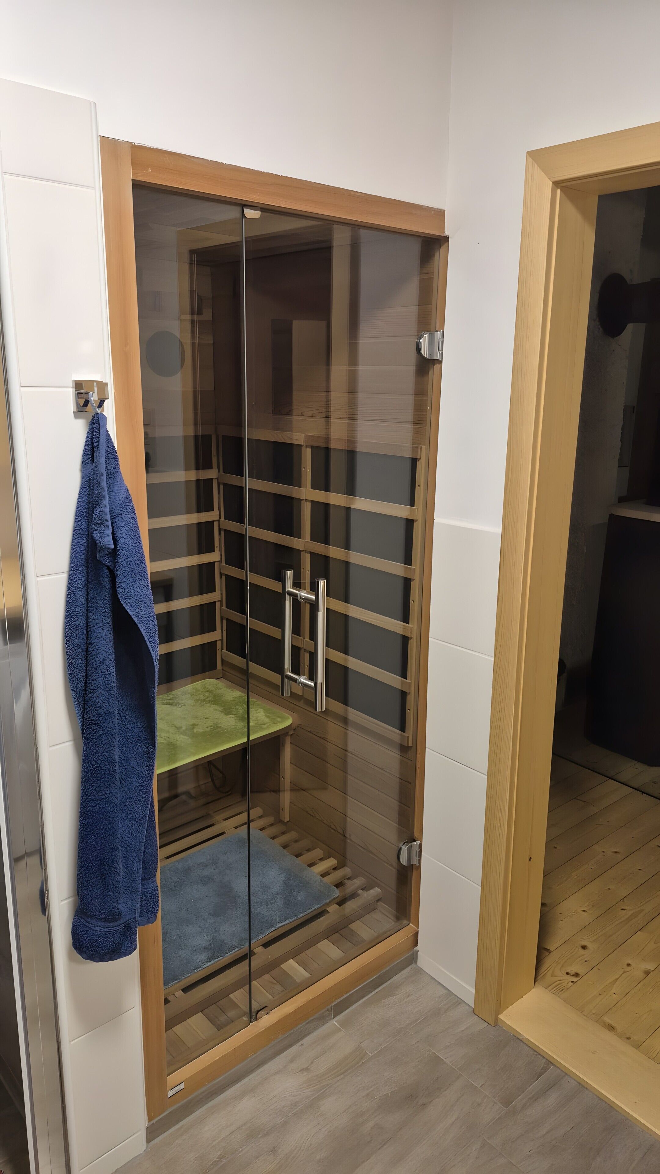 A glass-enclosed shower area with a wooden frame, a towel hanging on the wall, and a green mat on the floor.