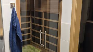 A glass-enclosed shower area with a wooden frame, a towel hanging on the wall, and a green mat on the floor.