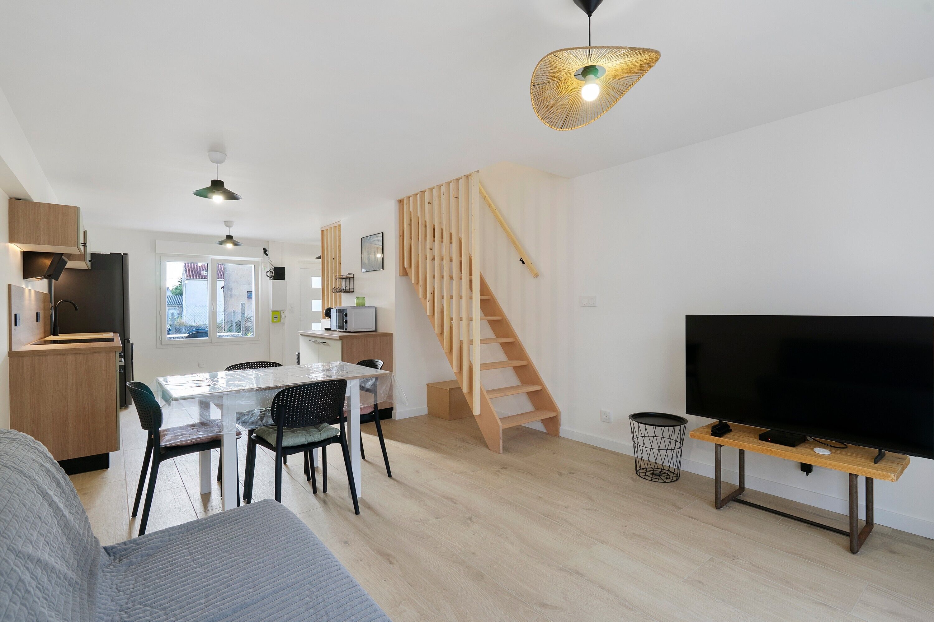 A modern apartment with a dining area, kitchen, staircase, and a living room with a flat-screen TV.