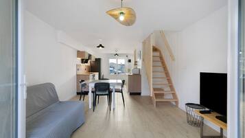 A modern living space with a sofa, dining table, chairs, a TV, and a staircase.