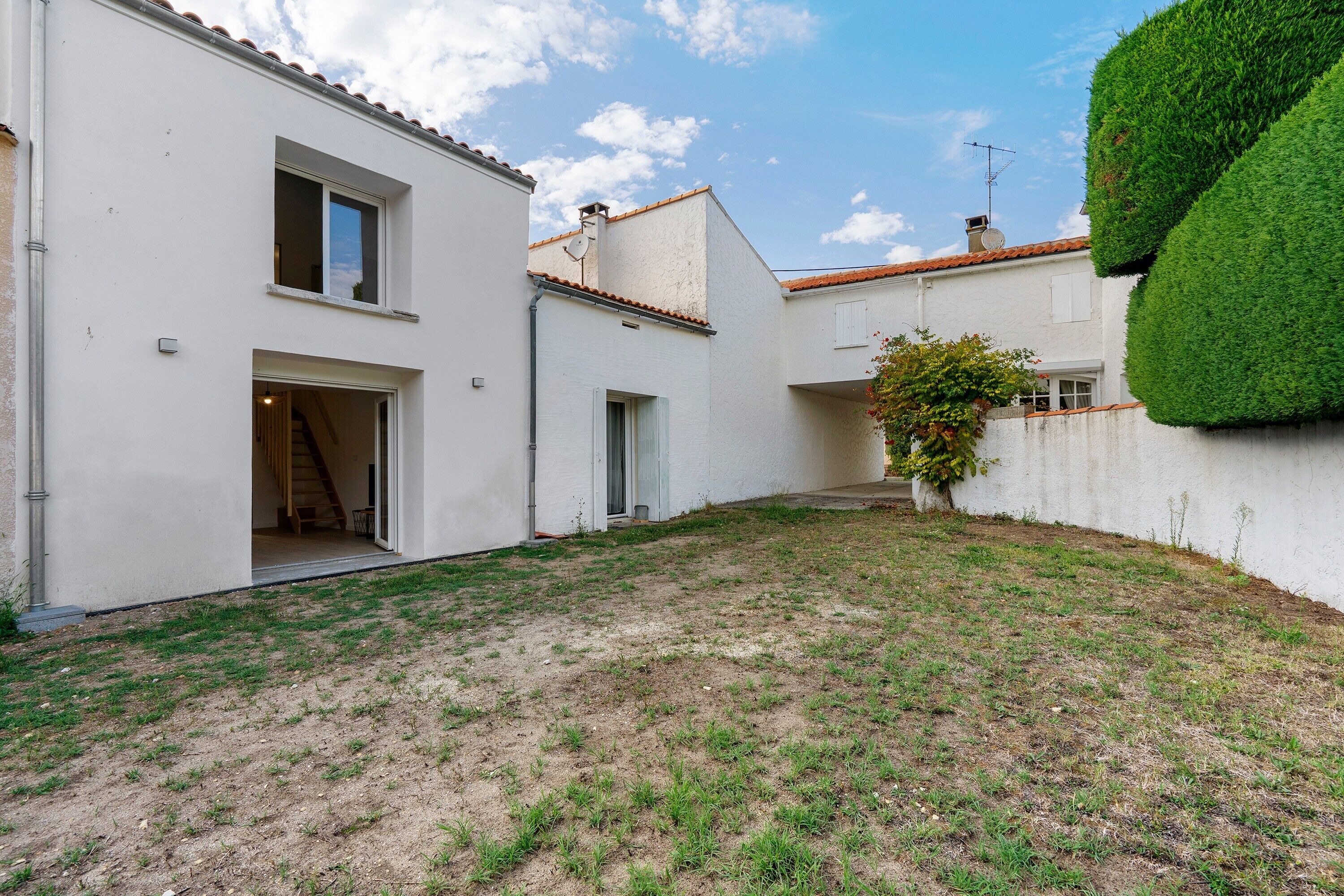Una propiedad residencial con un patio empedrado, una escalera que conduce a un nivel superior y un seto bien recortado.