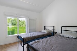 A bedroom with two single beds, a large window with a view of a green garden, and a ceiling with a skylight.
