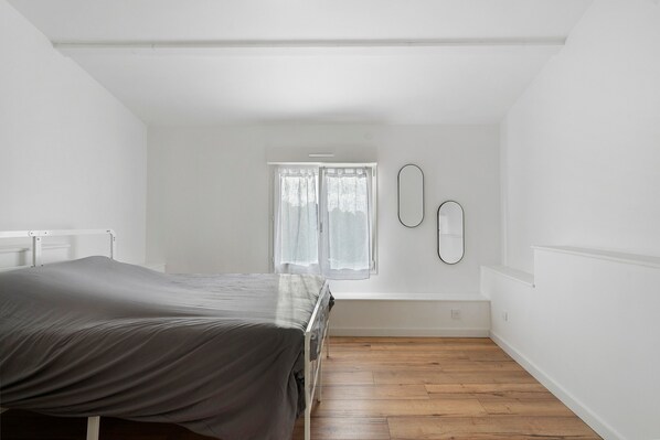 A bedroom with a bed, a window with curtains, and a wooden floor.