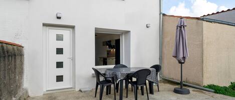 Un edificio blanco con puerta, ventana y un patio con mesa y sillas.
