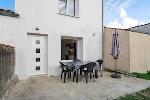A white building with a door, a window, and a patio area with a table and chairs.