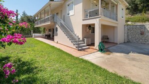 Ein zweistöckiges Haus mit Balkon, einer Treppe und einem Garten mit rosa Blumen.