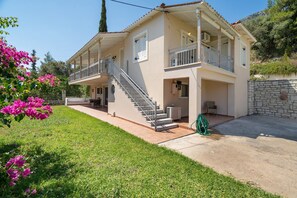 Ein zweistöckiges Haus mit Balkon, einer Treppe und einem Garten mit rosa Blumen.